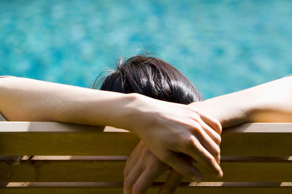 Woman relaxing in white lounge chair overlooking crystal clear turquoise swimming pool water