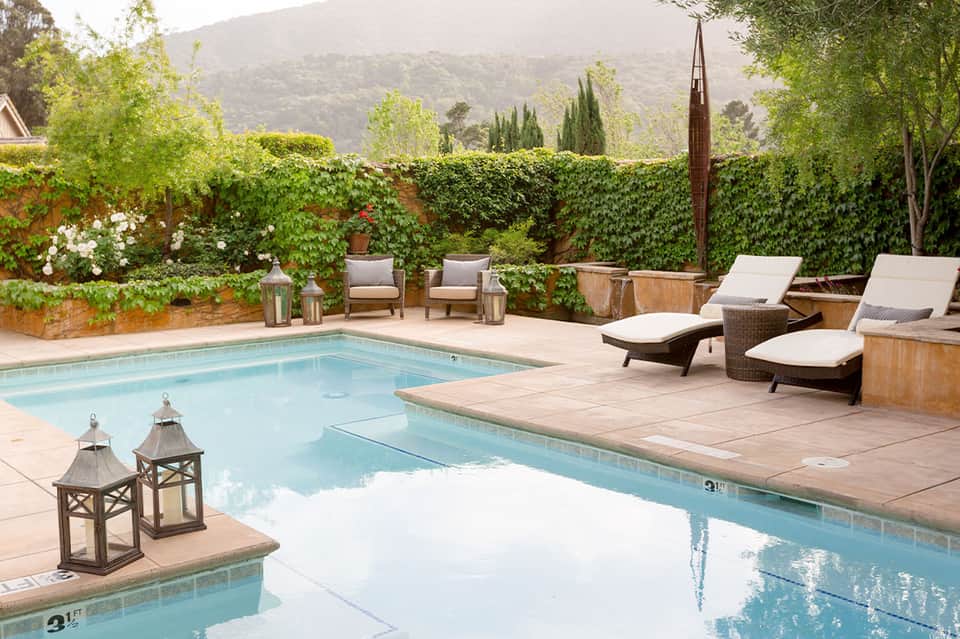 Luxury resort pool surrounded by ivy-covered walls, lounge chairs, mountain views, and lanterns