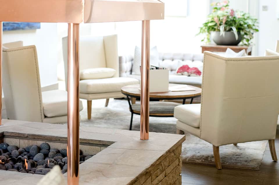 Elegant indoor lounge with fireplace, copper pergola, and cream-colored furnishings