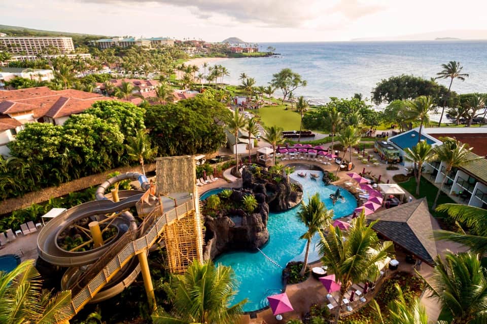 Aerial view of tropical resort with multiple pools, water slides, lush landscaping, and ocean