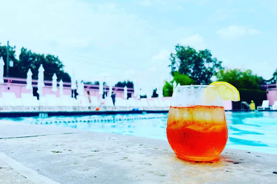 Red tropical cocktail with lime garnish on poolside, resort buildings and lap pool visible in background