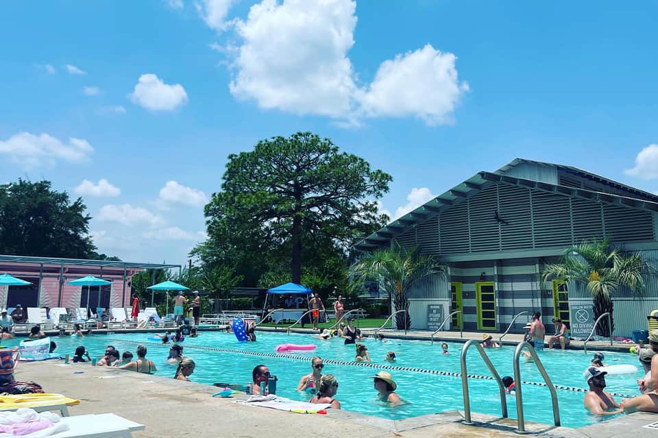 Community swimming pool with lap lanes, umbrellas, changing facilities, and visitors