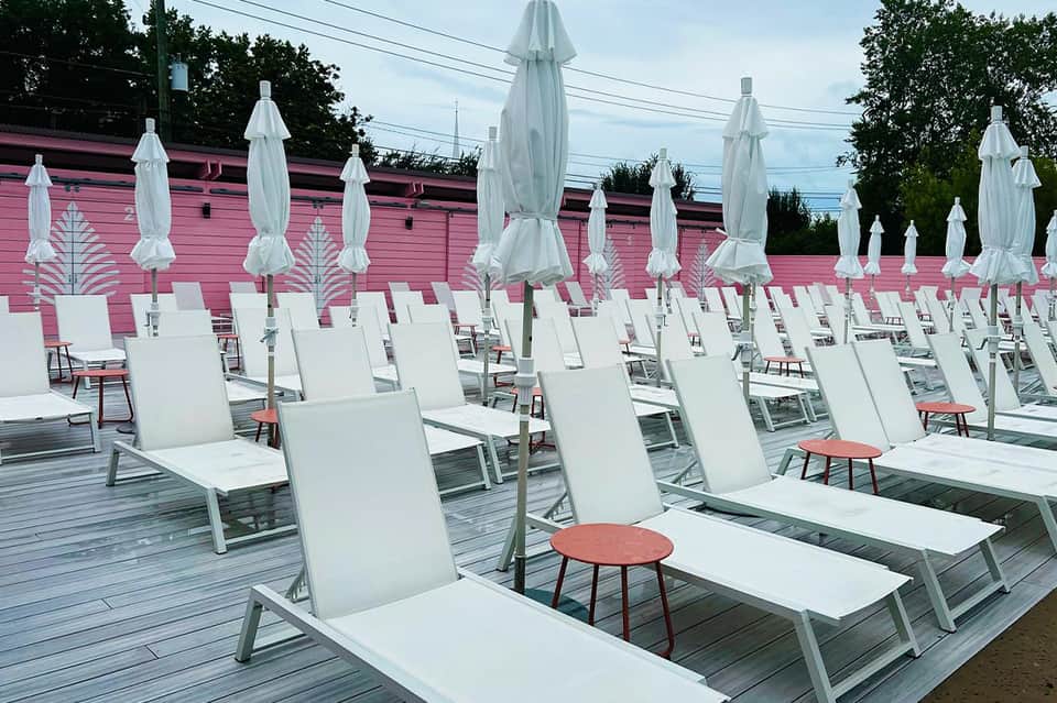 Beach club with white lounge chairs, closed umbrellas, and pink building backdrop