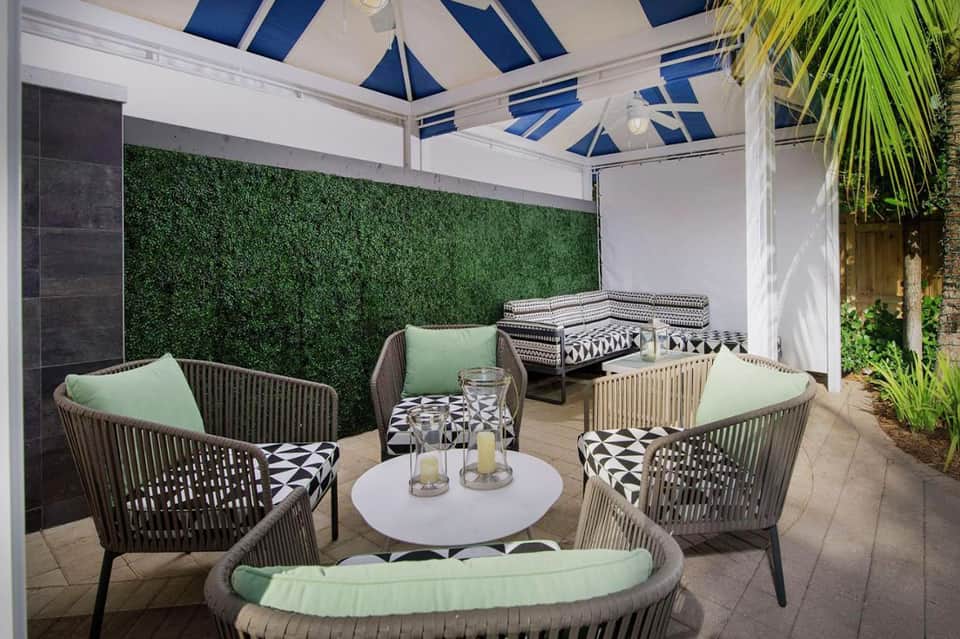 Private poolside cabana with blue striped retractable roof, modern patio furniture, and manicured landscaping