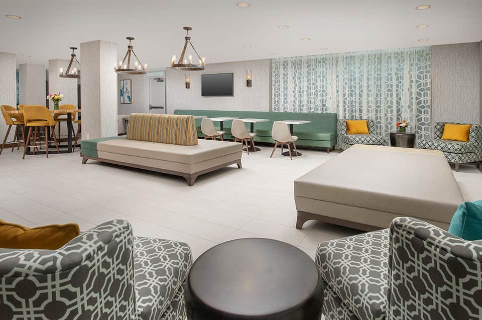Contemporary hotel lobby lounge with green sofa, patterned chairs, and pendant lighting