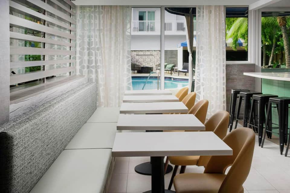 Resort dining area with window seating overlooking pool, featuring tan chairs and modern decor