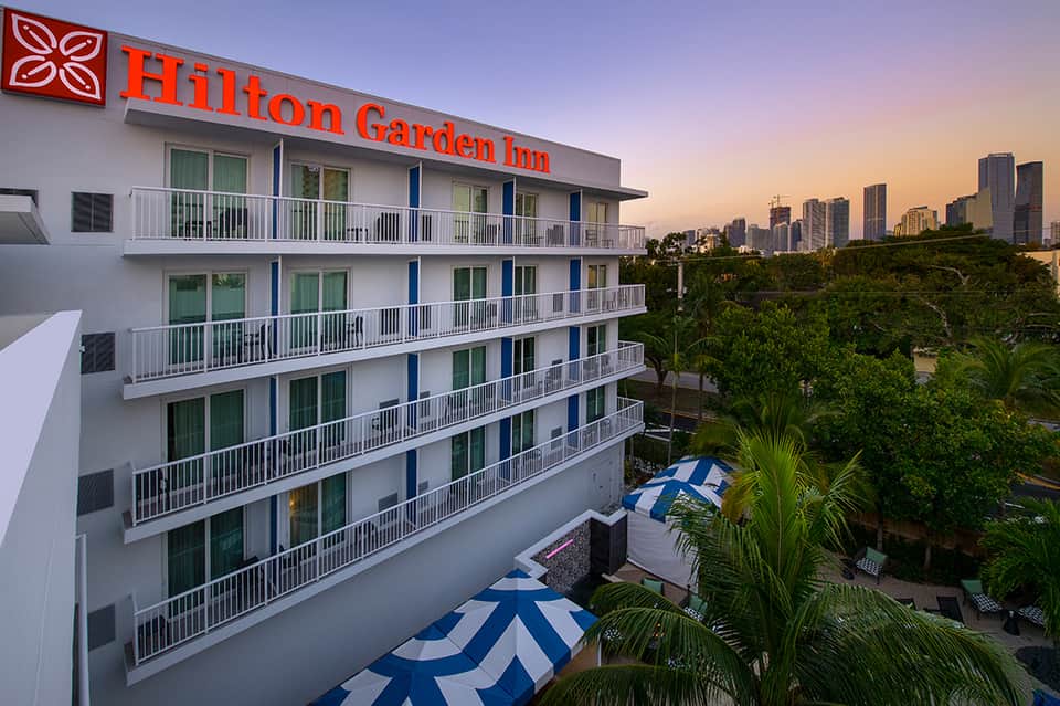 Hilton Garden Inn exterior at sunset with downtown city skyline visible in background