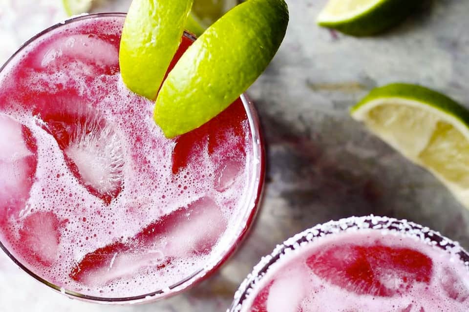 Pink margarita with salt rim and lime wedges, served over ice