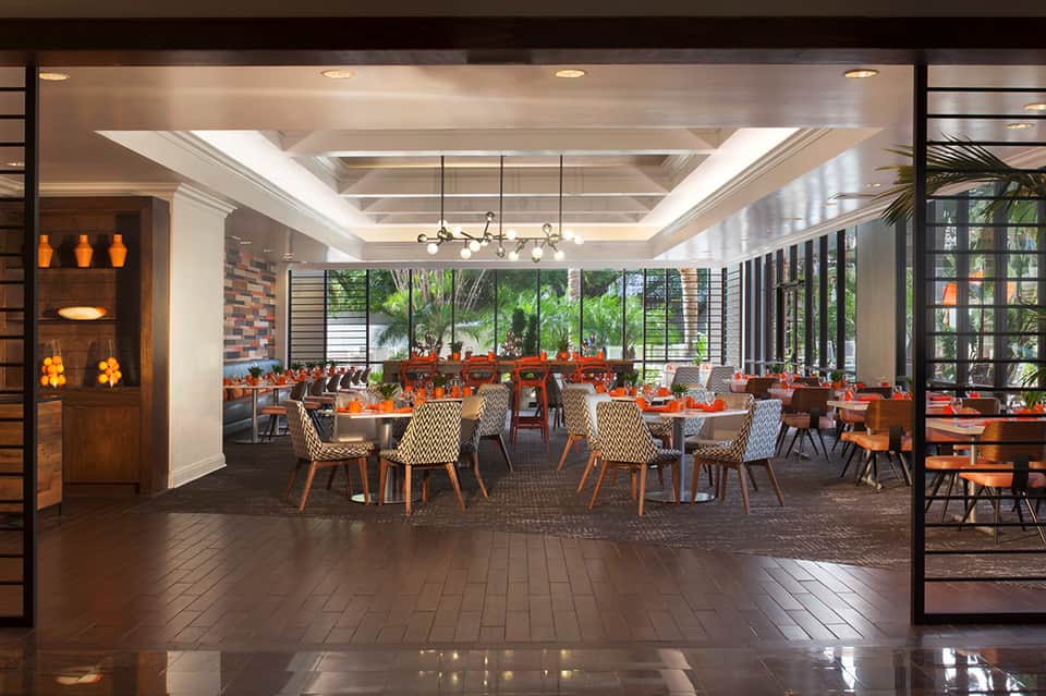 Modern hotel restaurant interior with tables, orange accents, and floor-to-ceiling windows