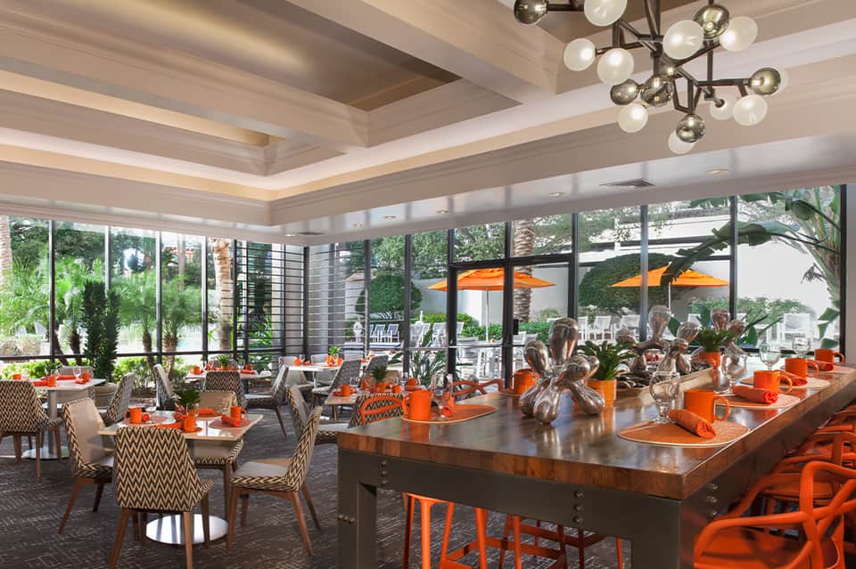 Elegant dining room with orange accents, modern lighting, and floor-to-ceiling windows