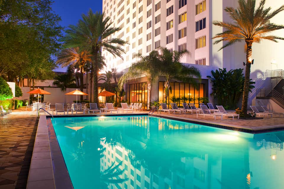 Illuminated resort pool at night with palm trees and hotel building
