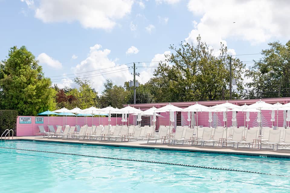 Outdoor swimming pool with turquoise water, white lounge chairs, and pink poolside cabana