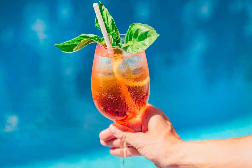 Tropical cocktail with mint garnish held against bright blue ocean background