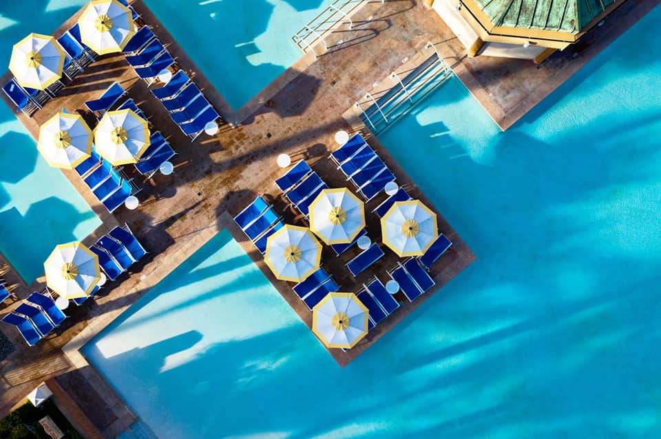 Aerial view of beach with blue and white umbrellas arranged on wooden deck beside turquoise water