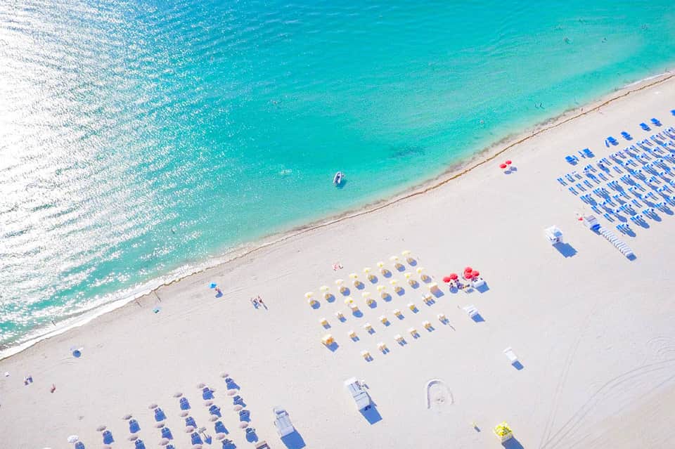 Aerial view of pristine beach with turquoise water and rows of blue beach umbrellas and loungers