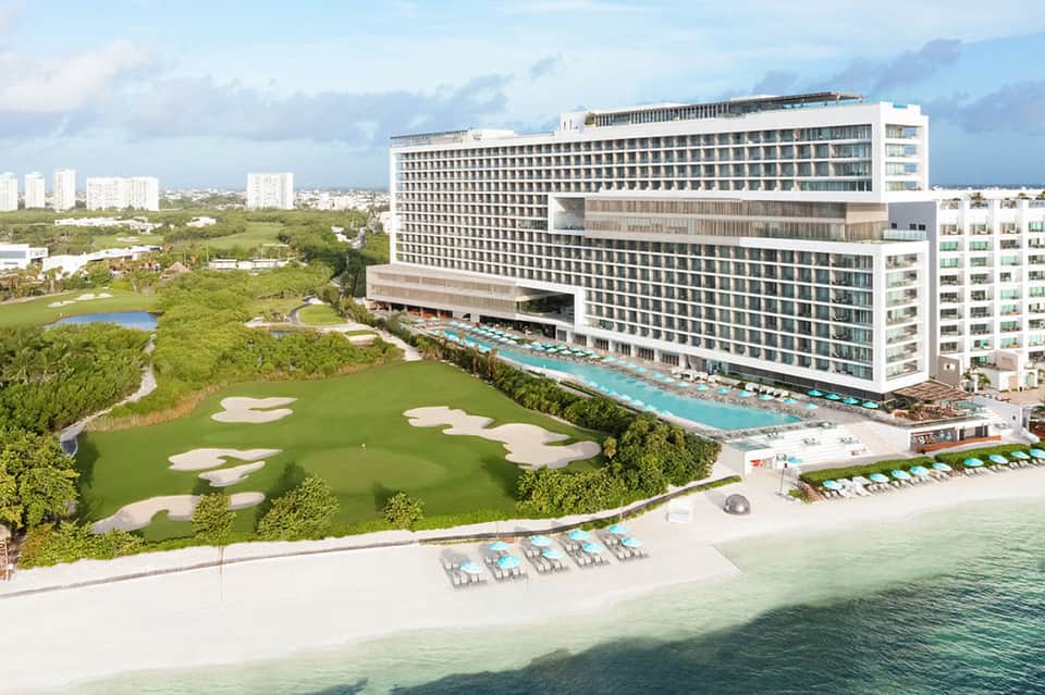 Beachfront resort exterior with modern architecture, lazy river, golf course, and turquoise water