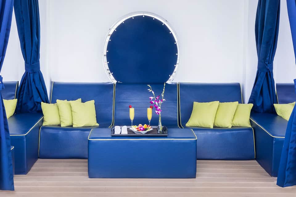 Modern pool cabana with blue seating, yellow pillows, and circular blue neon mirror accent