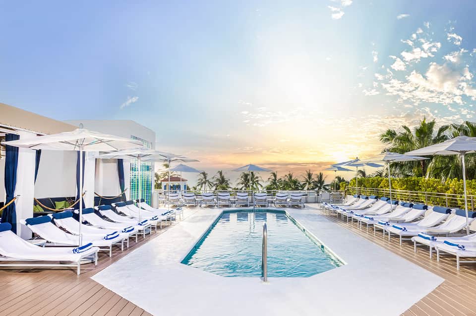 Luxury rooftop pool deck with cabanas, loungers, umbrellas, and sunset views