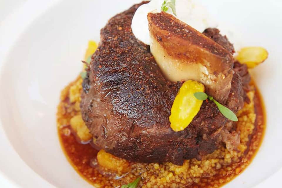 Fine dining plated dish with seared meat, foie gras, yellow garnish on white plate with sauce