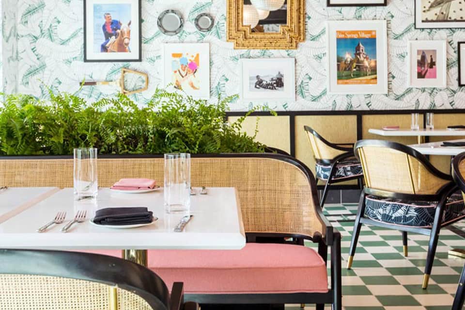 Casual restaurant dining area with fern wallpaper, gallery wall, and rattan seating