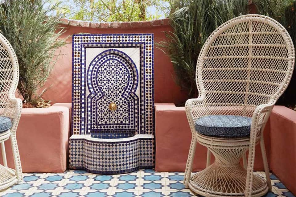 Moroccan-style courtyard with decorative blue and white mosaic fountain, rattan peacock chairs, terracotta walls