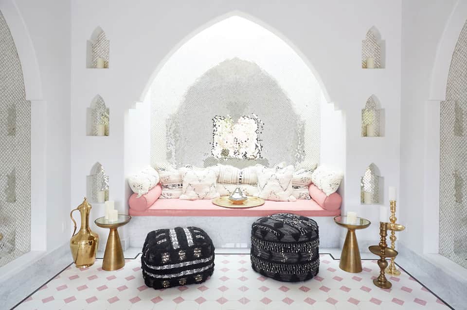 Glamorous white room with arched alcove, pink seating, decorative poufs, and gold accents
