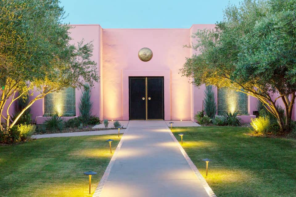 Pink modern building entrance with illuminated pathway and landscaping