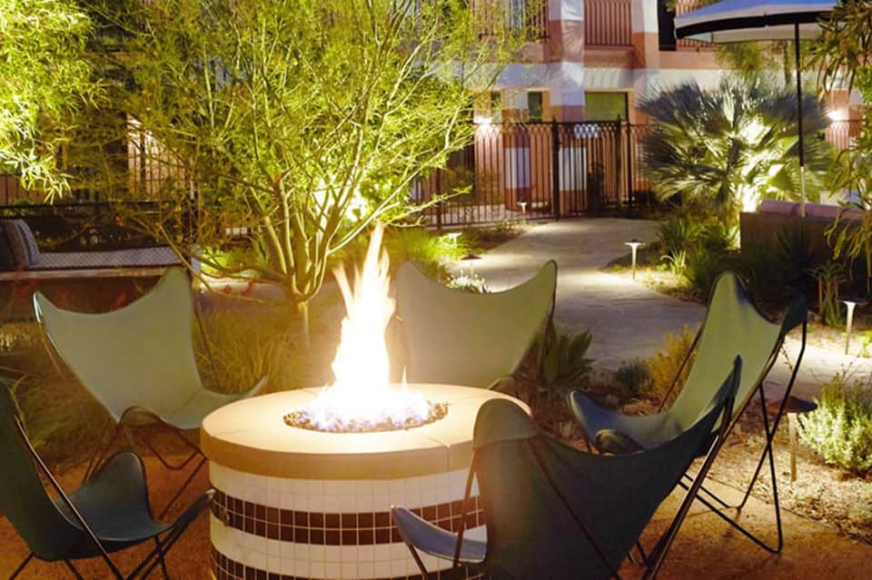 Outdoor seating area at night with fire pit, illuminated trees, modern chairs, and Mediterranean architecture