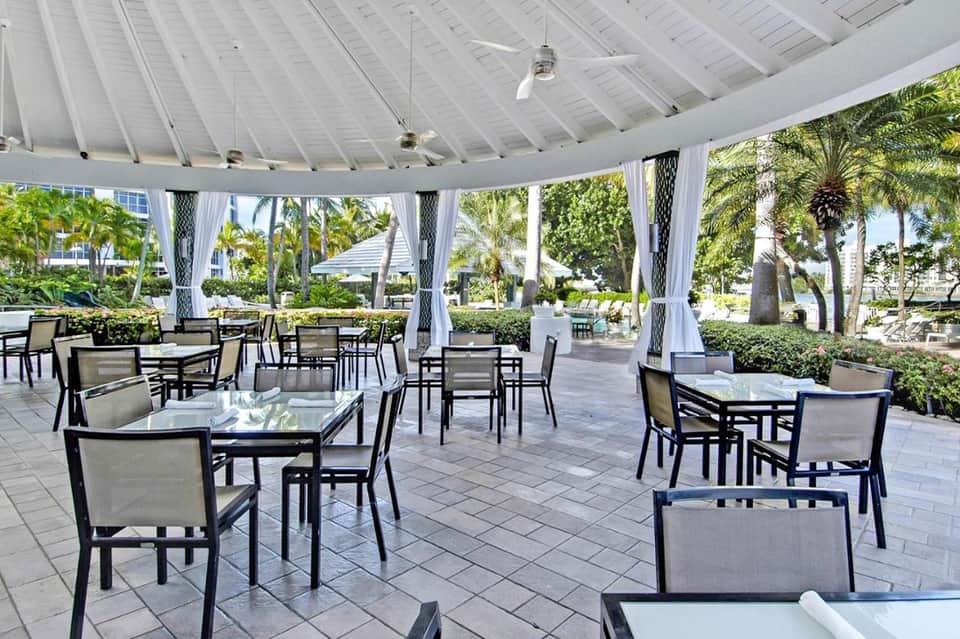 Covered outdoor dining pavilion with tables, chairs, and palm trees