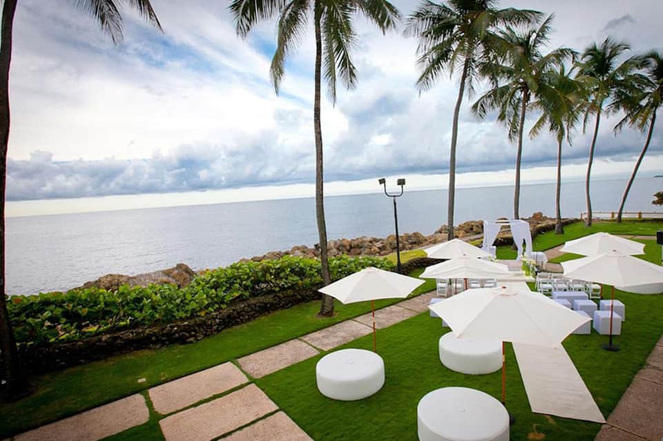 Beachfront lawn setup with white lounge furniture and palm trees at dusk