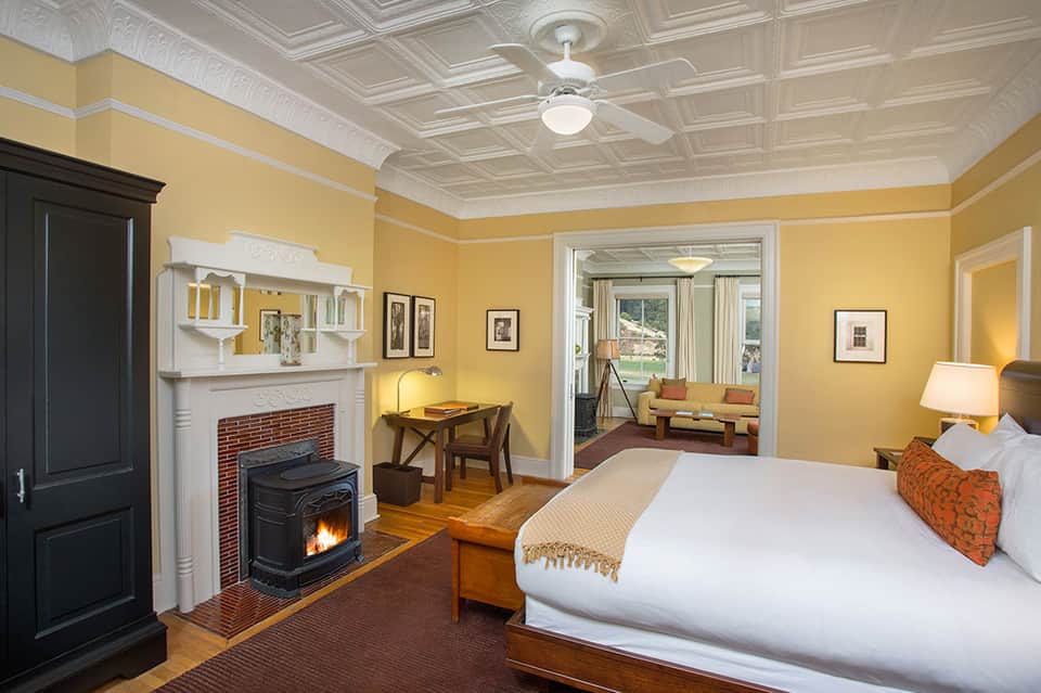Luxury bedroom with fireplace, yellow walls, wooden desk, and sitting area with windows