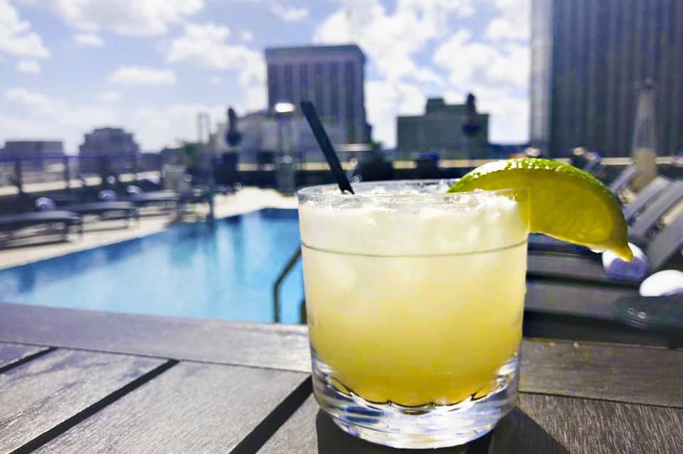 Citrus cocktail with lime wheel on rooftop bar overlooking city skyline and pool