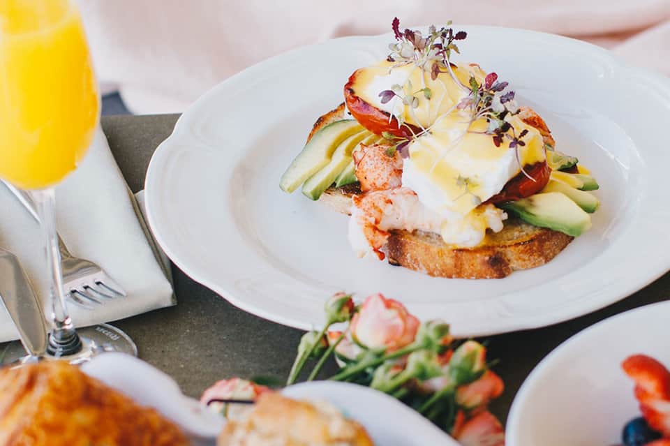 Gourmet eggs benedict with asparagus, hollandaise sauce, fresh flowers, and mimosa on white plate