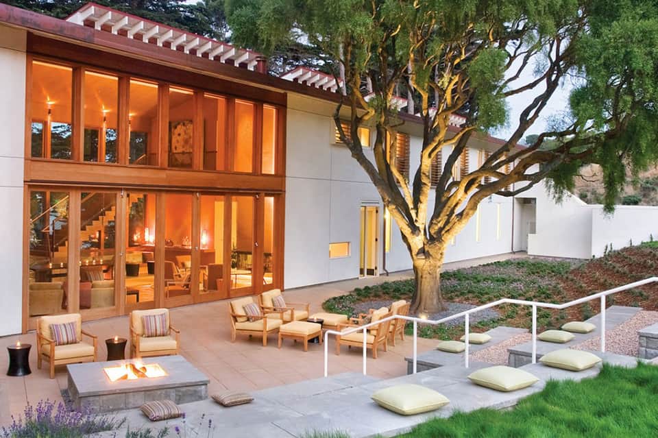 Modern residential patio with fireplace, wooden furniture, and evening outdoor lighting