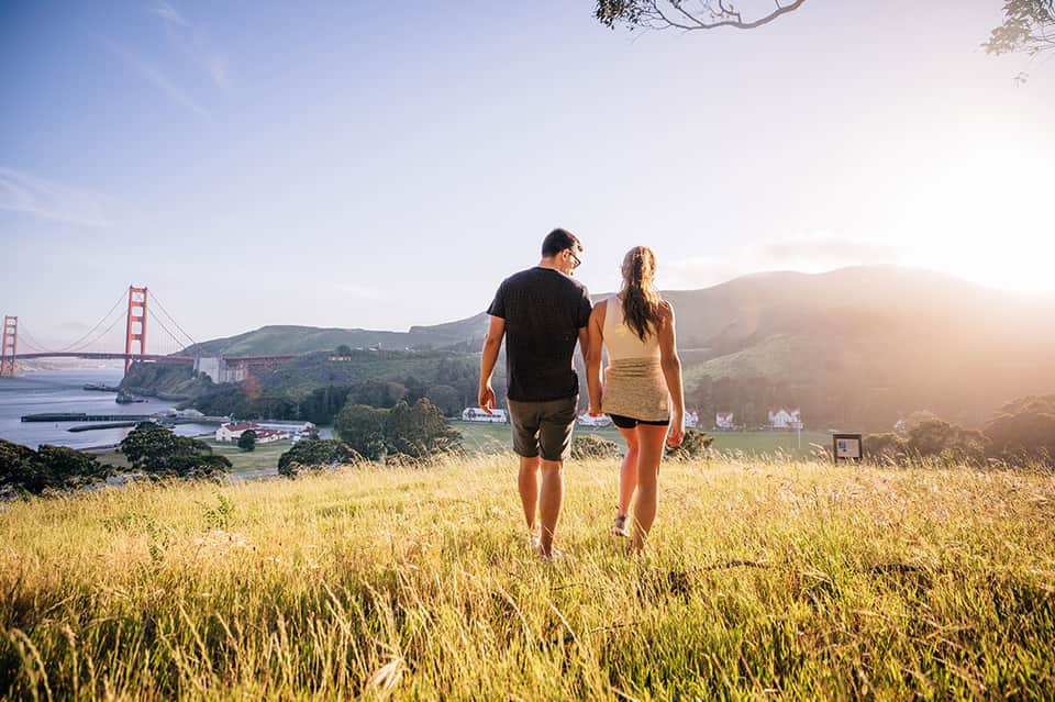 Couple jogging on grassy hillside overlooking Golden Gate Bridge and San Francisco Bay at sunset