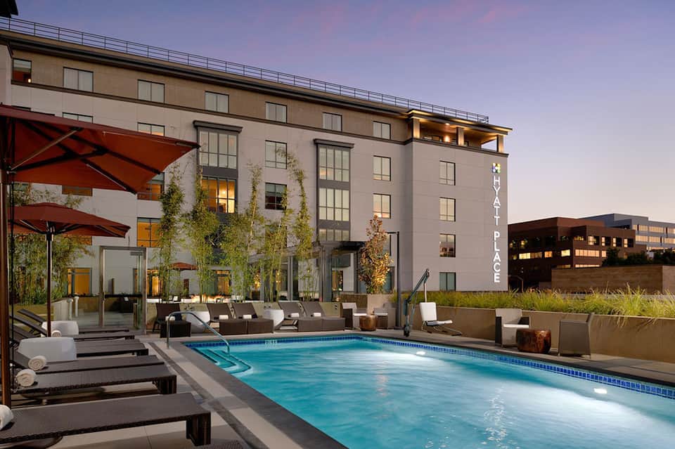 Modern hotel pool deck at dusk with lounge chairs, red umbrellas, and illuminated building