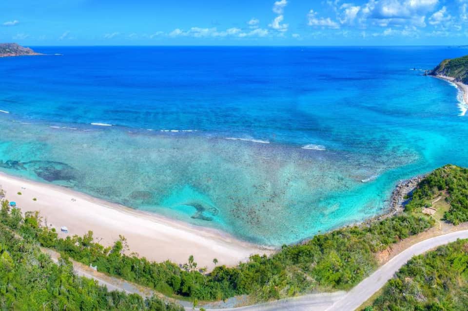 Pristine turquoise cove with white sandy beach, crystal clear water, rocky cliffs, and lush Mediterranean vegetation