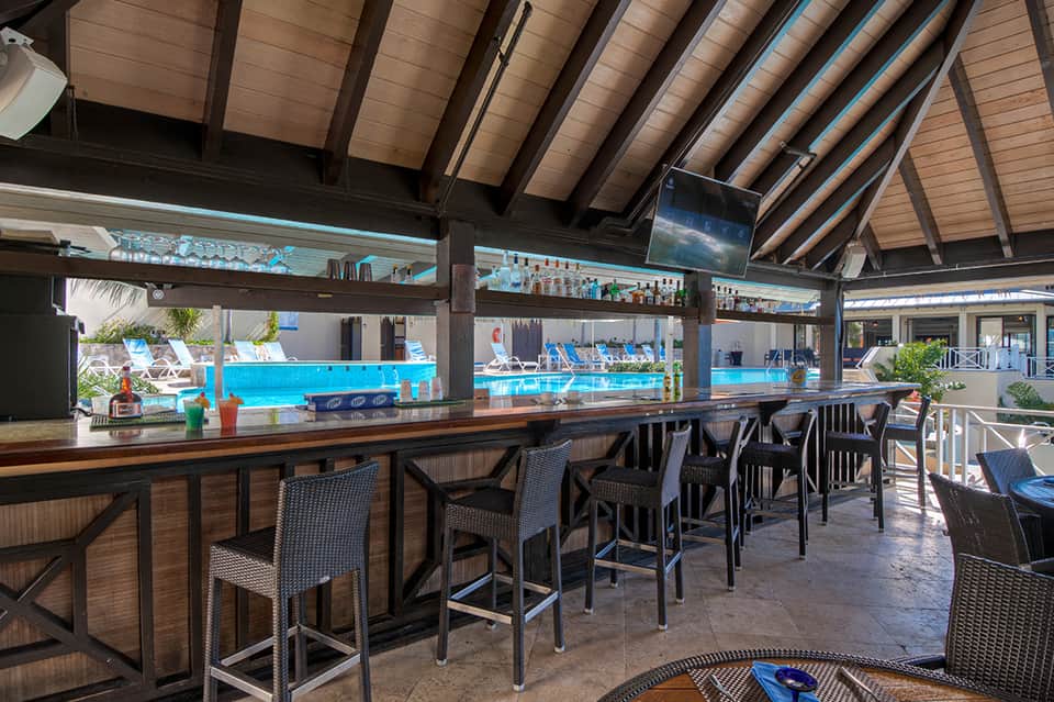 Covered pool bar with wood and metal structure overlooking sparkling resort swimming pool and lounging area