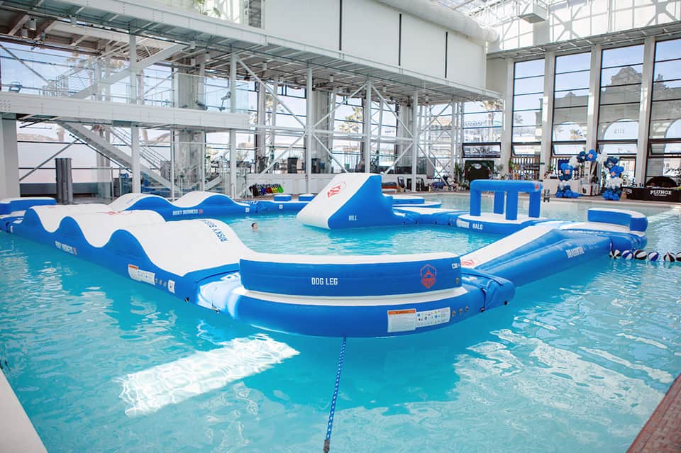 Indoor aquatic facility with wave pool, blue and white inflatable obstacles and obstacles