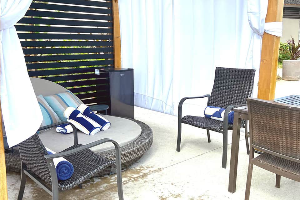 Outdoor lounge area with rattan chairs, striped pillows, sheer white curtains, and wooden privacy screen