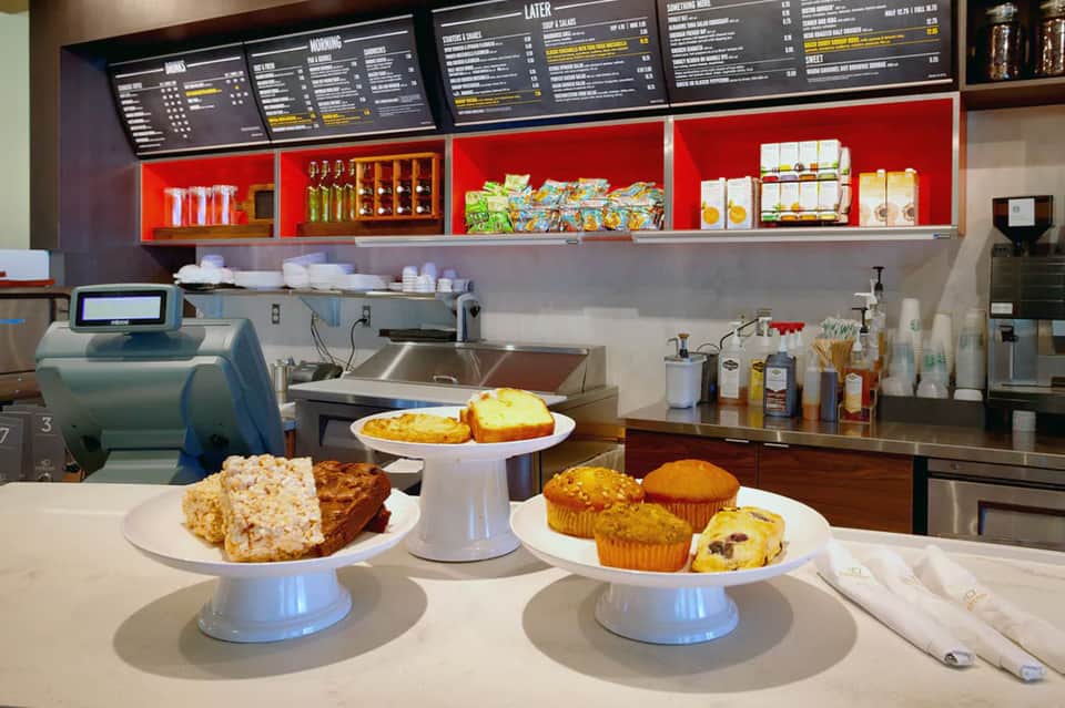 Coffee shop counter with pastries, muffins, and menu boards displayed on shelving