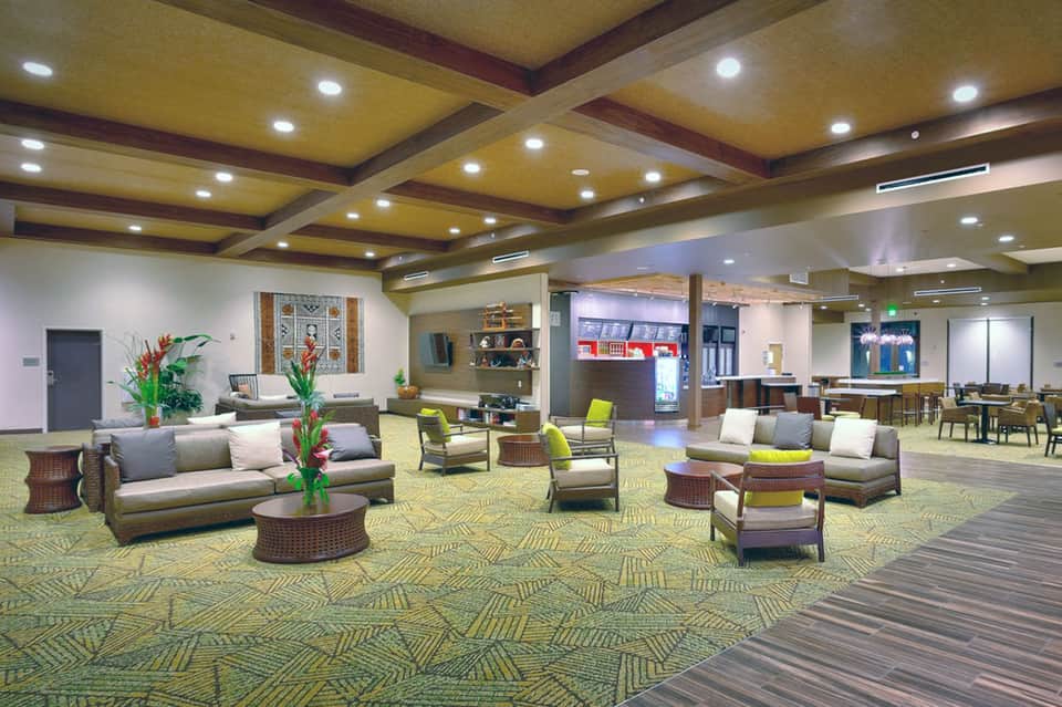 Modern hotel lobby with woven furniture, green accents, coffered ceiling, and spacious layout