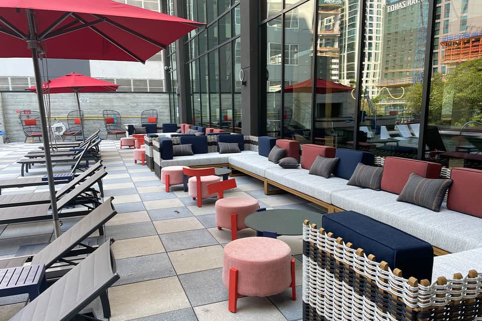 Modern rooftop terrace with red umbrellas, navy and coral seating, and city skyline views