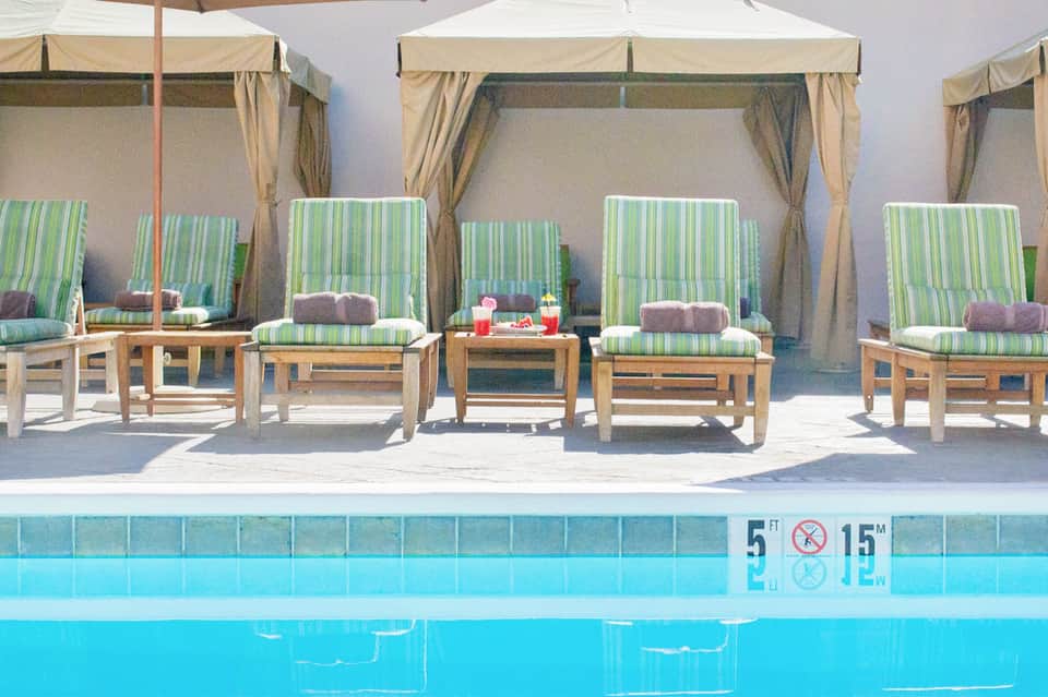 Poolside lounge area with green striped cabanas, white umbrellas, and crystal blue water