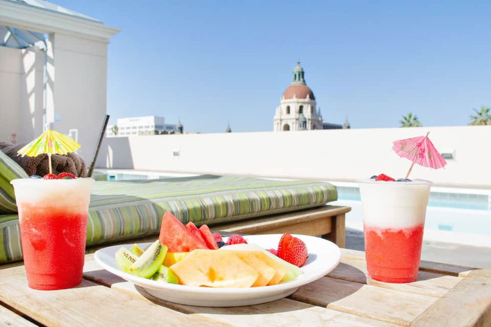 Rooftop poolside dining with cocktails, fresh fruit, and city skyline views featuring a dome-topped building