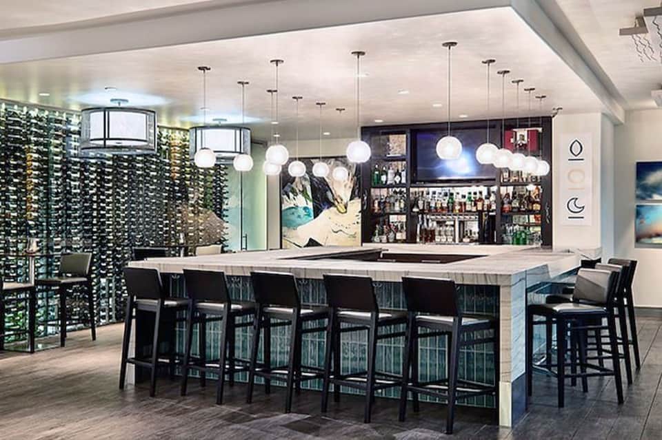 Modern hotel bar with floating pendant lights, wine display wall, marble counter, and bar seating