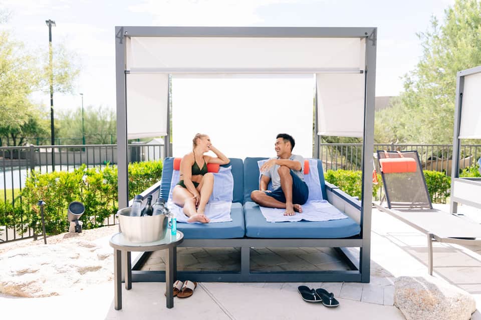 Couple relaxing on modern daybed with retractable shade near pool and landscape
