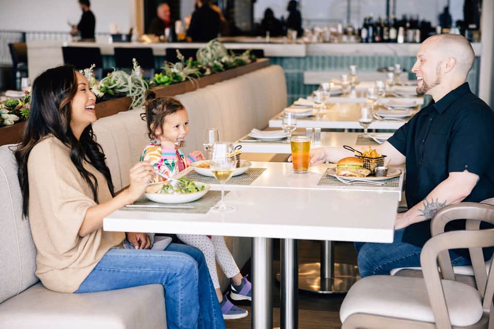 Family dining together at modern restaurant with white table and plant wall backdrop