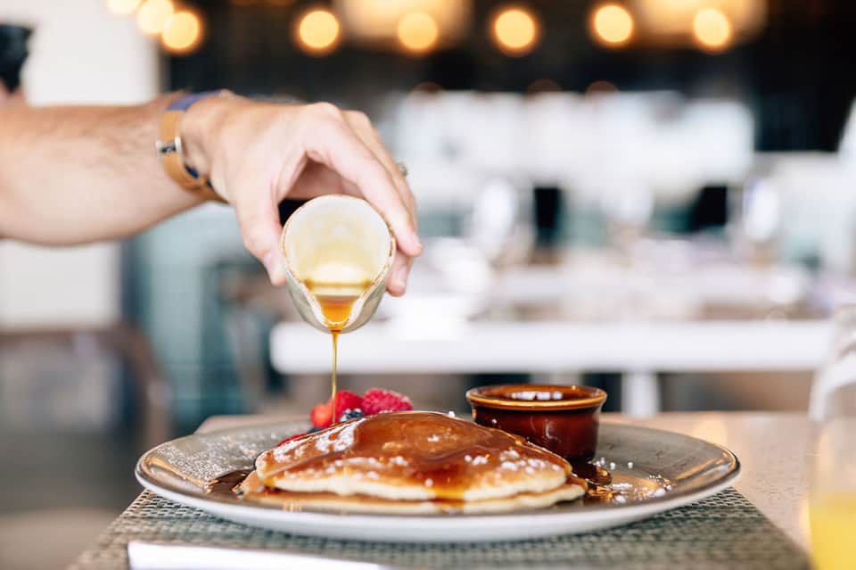 Honey being drizzled onto pancakes at elegant restaurant table with warm ambiance