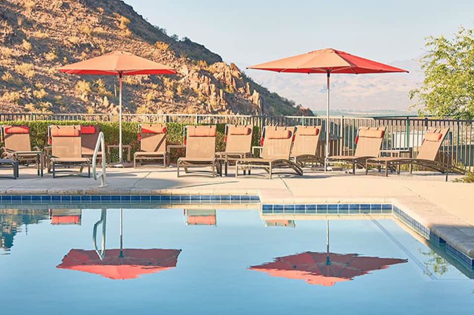 Resort pool with red umbrellas and lounge chairs against mountain backdrop
